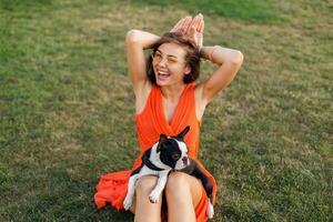 Jeune content souriant femme dans Orange robe ayant amusement en jouant avec chien dans parc photo