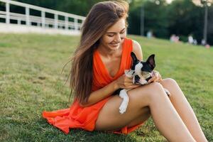 Jeune content souriant femme dans Orange robe ayant amusement en jouant avec chien dans parc photo