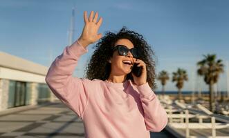 Jeune jolie frisé femme dans des lunettes de soleil sur été vacances avec téléphone photo