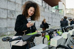 jolie frisé femme location une vélo dans rue avec un app photo