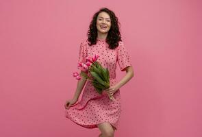 jolie Jeune femme posant isolé sur rose studio Contexte avec tulipes fleurs photo