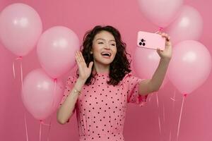jolie Jeune femme posant isolé sur rose studio Contexte avec rose air ballons et téléphone intelligent photo
