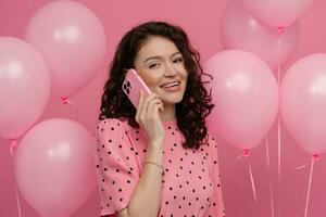 jolie Jeune femme posant isolé sur rose studio Contexte avec rose air ballons et téléphone intelligent photo