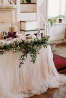 le présidium des jeunes mariés dans la salle de banquet du restaurant est décoré de bougies et de plantes vertes photo