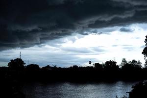 silhouette de paysage d'arbres et tour électrique avec nuage de pluie dans le ciel lumineux se reflétant sur la surface de la rivière photo