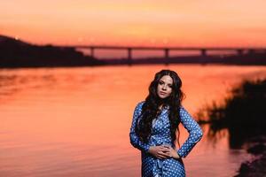 belle jeune fille aux longs cheveux ondulés noirs debout au bord de la rivière photo