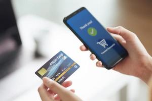 jeune femme tenant une carte de crédit et utilisant un téléphone intelligent pour les achats en ligne, les services bancaires sur Internet, le commerce électronique, dépenser de l'argent, travailler à domicile photo