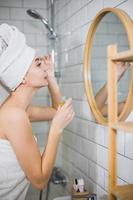 jeune femme en serviette blanche applique de l'huile hydratante sur la peau du visage. photo