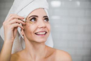 jeune femme en serviette blanche applique de l'huile hydratante sur la peau du visage. photo