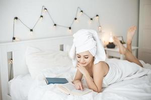jeune femme heureuse lisant un livre papier au lit.