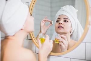 jeune femme en serviette blanche applique de l'huile hydratante sur la peau du visage. photo