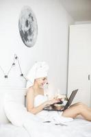 jeune femme travaillant dans un lit blanc à l'aide d'un ordinateur portable. photo
