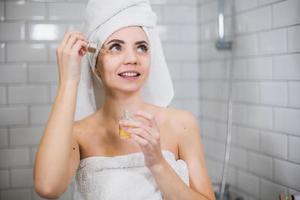 jeune femme en serviette blanche applique de l'huile hydratante sur la peau du visage. photo