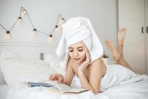 jeune femme heureuse lisant un livre papier au lit.
