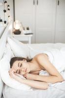 Jeune femme dormant paisiblement dans la chambre avec des draps frais blancs photo