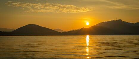 d'or ciel jette ses lueur sur le tranquille des eaux, où le majestueux montagnes Cadre le scène, se prélasser dans le chaud embrasse de le Soleil. photo