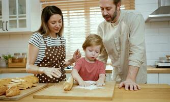 père et mère enseignement bébé fils pétrissage pâte sur cuisine compteur à maison. Parents et garçon enfant prendre plaisir et amusement à l'intérieur activité cuisine ensemble. photo