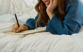 content Jeune femme pose sur lit et l'écriture dans journal à chambre à coucher. photo