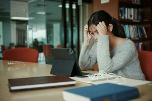 asiatique étudiant femme lis livres dans bibliothèque à université. Jeune fille stress fatigué avoir problème tandis que étude dur. tristesse concept photo