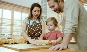 père et mère enseignement bébé fils pétrissage pâte sur cuisine compteur à maison. Parents et garçon enfant prendre plaisir et amusement à l'intérieur activité cuisine ensemble. photo