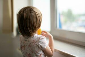 une petit enfant regards en dehors le fenêtre de derrière photo