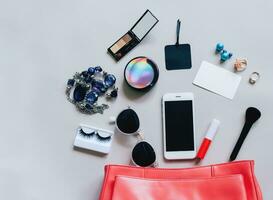 mise à plat de sac femme en cuir rose ouvert avec des cosmétiques, des accessoires, une carte d'étiquette et un smartphone sur fond gris avec espace de copie photo