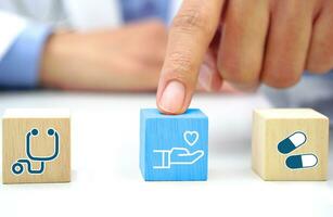 doigt de médecin émouvant le bleu en bois bloquer cube avec soins de santé médical icône symbole. médical et santé concept. photo