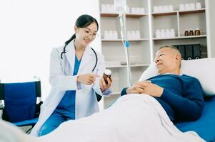 asiatique médecin dans blanc costume prendre Remarques tandis que discuter et asiatique âgé, homme patient qui mensonge sur lit avec recevoir saline Solution dans hôpital photo