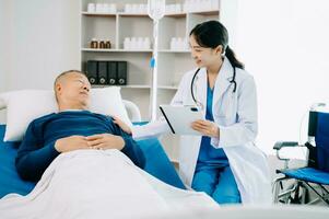 asiatique médecin dans blanc costume prendre Remarques tandis que discuter et asiatique âgé, homme patient qui mensonge sur lit avec recevoir saline Solution dans hôpital photo