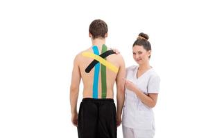 Jeune femme physiothérapeute appliquant un ruban physio spécial sur le dos de l'homme