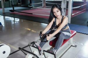 aptitude asiatique femmes performant Faire des exercices formation avec aviron machine dans sport Gym intérieur et aptitude santé club avec des sports exercice équipement salle de sport. photo