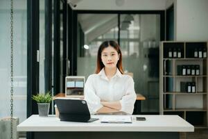 femme d'affaires asiatique travaillant au bureau avec des documents de travail sur bloc-notes, tablette et ordinateur portable photo