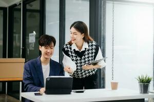 un collègue d'affaires asiatique présente et explique et utilise un ordinateur portable et une tablette. travail d'équipe, équipe de marketing financier, assis dans un bureau moderne. photo