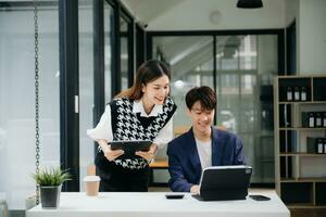 deux asiatique femme d'affaires et homme discuter investissement projet travail et Planification stratégie avec tablette portable ordinateur dans bureau. photo