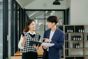 un collègue d'affaires asiatique présente et explique et utilise un ordinateur portable et une tablette. travail d'équipe, équipe de marketing financier, assis dans un bureau moderne. photo