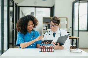 deux scientifique ou médical technicien fonctionnement, ayant une médical discuter réunion avec un asiatique Sénior femelle scientifique superviseur dans le laboratoire avec en ligne en lisant, tester échantillons photo