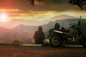 femme séance à côté de moto à magnifique point de vue et à la recherche à le coucher du soleil scène photo