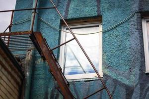 Fenêtre blanche dans un mur texturé bleu avec des escaliers en métal rouillé en dessous photo