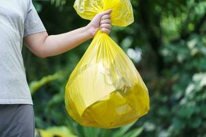 homme bénévole charité en portant des ordures Jaune sac et Plastique bouteille des ordures pour recyclage nettoyage photo