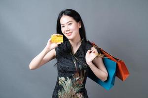 une femme asiatique porte une robe traditionnelle chinoise avec un sac à provisions et une carte de crédit photo