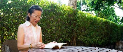 femme asiatique âgée portant des lunettes assise dans le livre de lecture de jardin en été. développement personnel et nouveau concept de mode de vie normal photo
