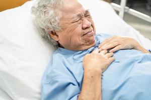 Une patiente âgée ou âgée d'origine asiatique ressent une douleur à la poitrine et au cœur sur son lit dans une salle d'hospitalisation photo