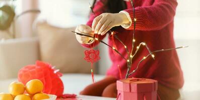 asiatique femme décoré maison pour chinois Nouveau année célébrations. en mettant traditionnel pendentif à le chinois lunaire Nouveau année pour bien chance. chinois mot veux dire bénédiction photo