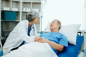 asiatique médecin dans blanc costume prendre Remarques tandis que discuter et asiatique âgé, homme patient qui mensonge sur lit avec recevoir saline Solution dans hôpital ou clinique. photo