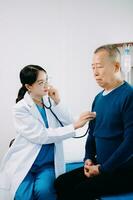 asiatique médecin dans blanc costume prendre Remarques tandis que discuter et asiatique âgé, homme patient qui mensonge sur lit avec recevoir saline Solution dans hôpital photo