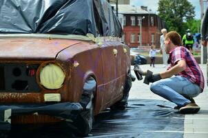 kharkov, ukraine - 27 mai 2017 festival d'art de rue. les jeunes gars dessinent des graffitis sur la carrosserie de la voiture dans le centre-ville. le processus de dessin de graffitis de couleur sur une voiture avec des aérosols photo