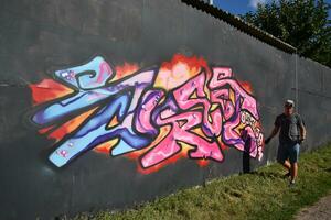 Jeune caucasien Masculin graffiti artiste dessin gros rue art La peinture dans bleu et rose tons photo