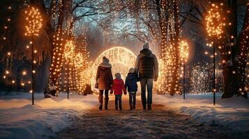 famille, Parents et les enfants dans une magnifique hiver jardin avec Noël lumières sur le des arbres dans le soir photo