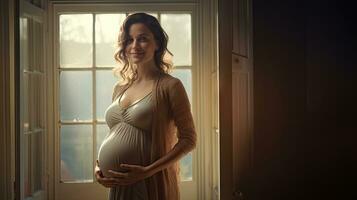 une Enceinte femme se tenait souriant dans le coin de le fenêtre avec lumière diffusion par le la fenêtre. photo