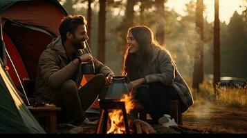 Jeune couple ayant une pique-nique séance près une feu de camp et tente boisson café dans le pin forêt photo